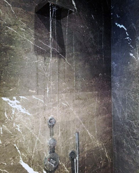 A marble-tiled shower with water cascading from a sleek square showerhead
