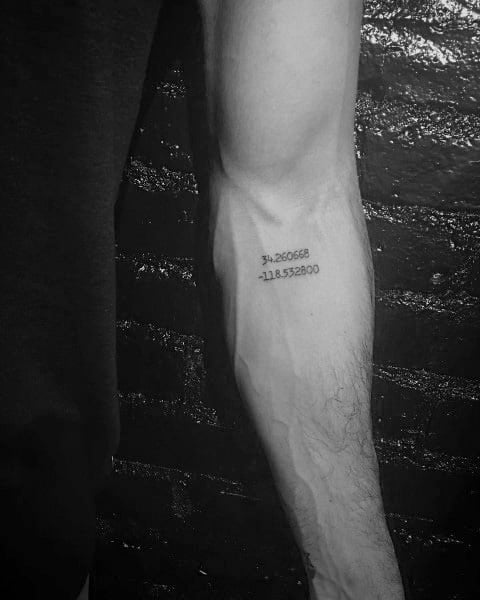 Minimalist coordinate tattoo on the forearm with simple black text, marking a significant location with a clean and subtle design.