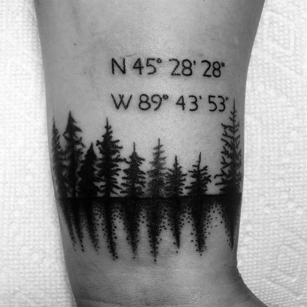 Forest coordinate tattoo on the wrist with bold black tree silhouettes and reflection shading, symbolizing a meaningful location in nature.