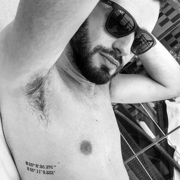 Minimalist coordinate tattoo on the ribcage with clean black lettering, marking a significant location with a sleek and subtle design.