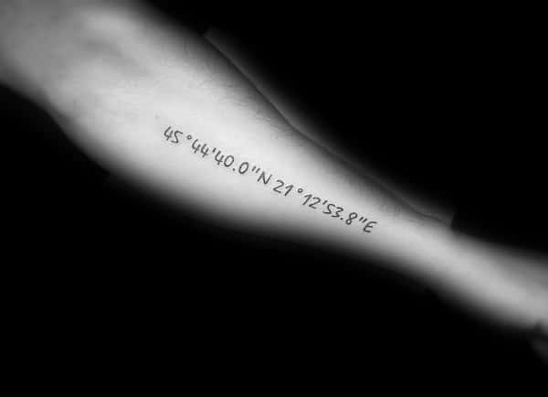 Simple and elegant coordinate tattoo on the forearm with clean black lettering, marking a significant location with a minimalist design.