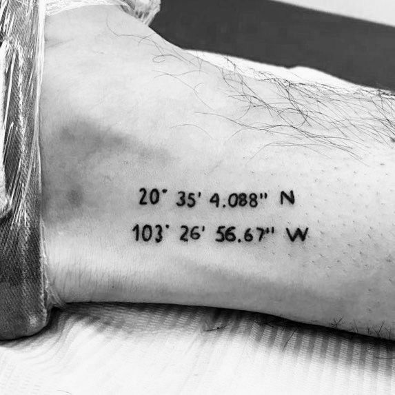 Minimalist coordinate tattoo on the ankle with clean black lettering, marking a significant location with a subtle and meaningful design.