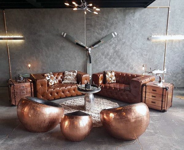 A bachelor pad features tufted brown leather couches with sleek copper chairs and accents, creating a bold industrial aesthetic.
