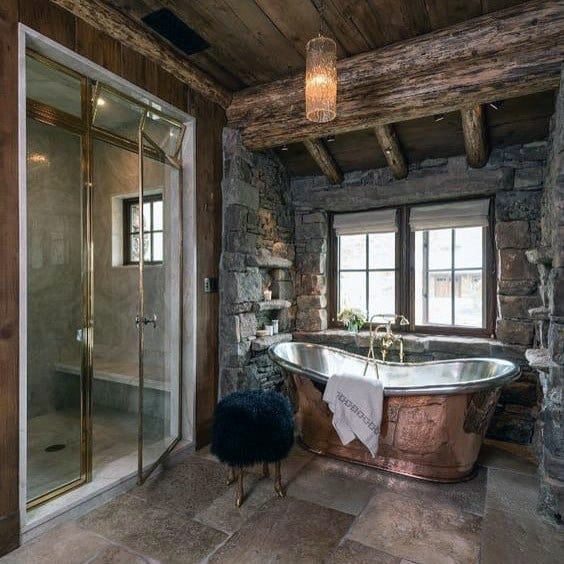 Rustic bathroom with a copper bathtub, stone walls, and elegant glass shower enclosure