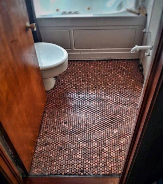 Bathroom with copper penny tile flooring, white tub, and wooden door detailing.