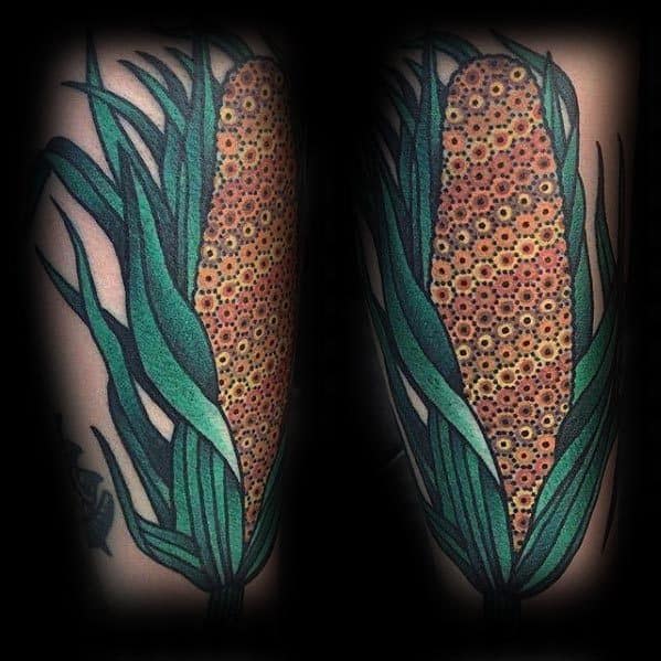 Bold and colorful tattoo of a corn cob with detailed kernels and flowing green husks, creating a striking design on the skin.