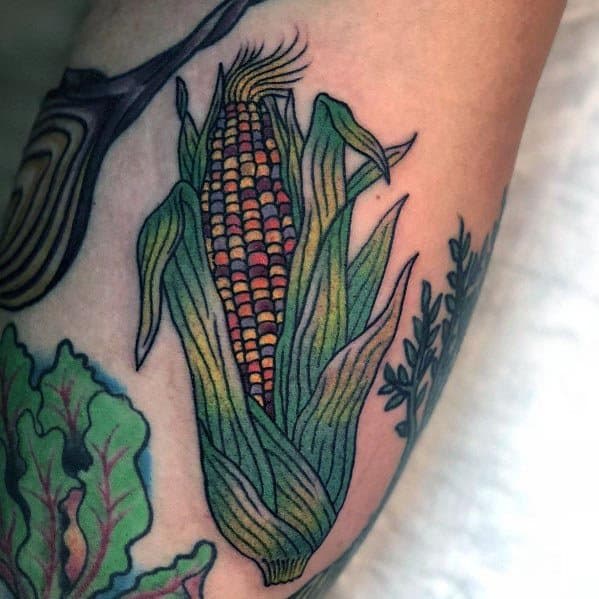 Vibrant tattoo of a detailed corn cob with green husks and multicolored kernels, surrounded by botanical elements for a natural look.