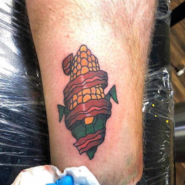 Playful tattoo of a corn cob wrapped in crispy bacon, featuring bold outlines and vibrant colors for a unique and creative design.