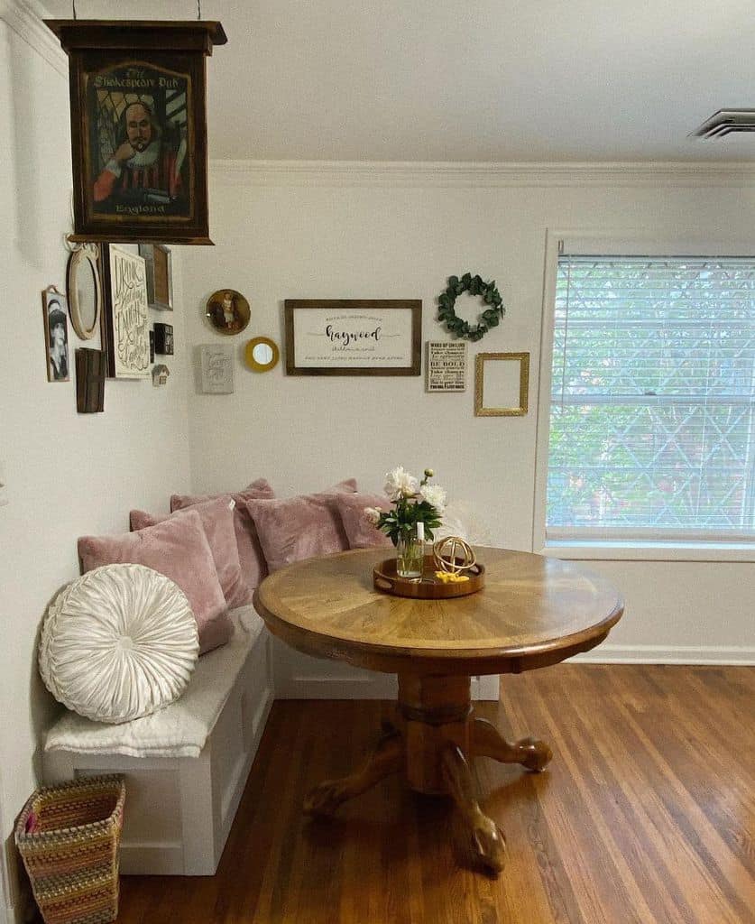 Cozy corner seating with a round wooden table, pink pillows, and wall art decor.