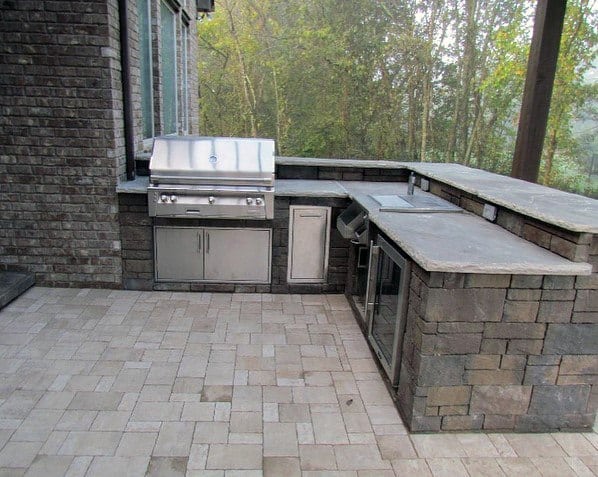 Outdoor kitchen with stone countertops, built-in grill, cabinets, all surrounded by lush trees