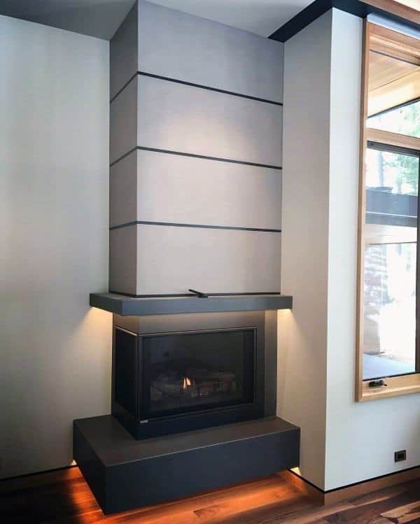 Modern corner fireplace with sleek concrete design, built-in lighting, and wooden flooring.