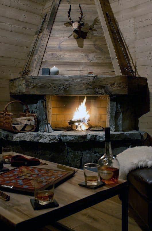 Rustic corner fireplace with wood hood, stone base, and cozy decor.