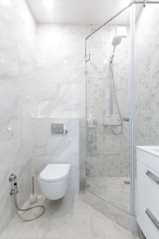 Modern bathroom with marble-effect tiles, glass shower, and wall-mounted toilet.