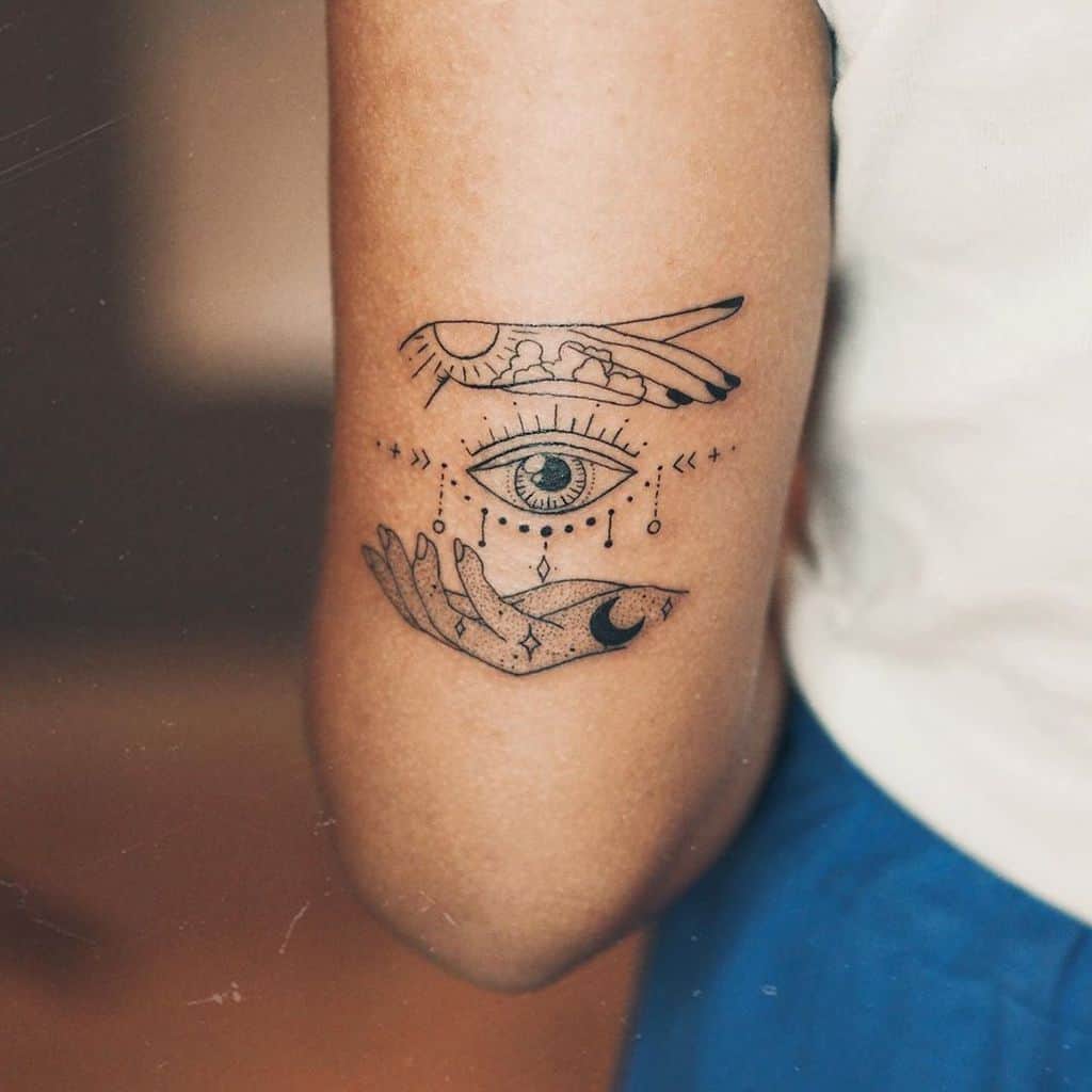 Minimalist tattoo of an all-seeing eye with celestial hands, delicate dot work, and fine lines on the arm.