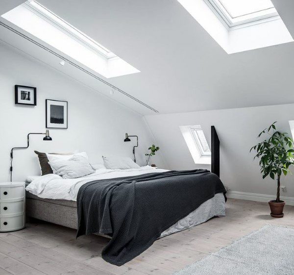 Cozy attic bedroom with skylights, white walls, black wall lamps, and a potted plant by the bed