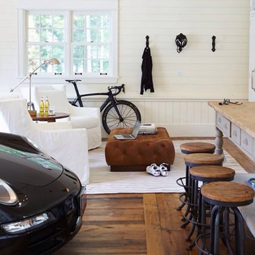 Stylish man cave with a car, bicycle, white chairs, ottoman, and bar stools on wooden flooring