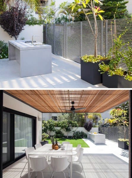 Modern outdoor patio with dining area, pergola, sleek kitchen counter, lush plants, and green lawn in the background