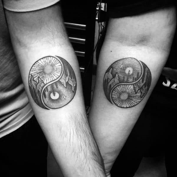 Matching forearm tattoos of a yin-yang design with mountain and sun elements, symbolizing harmony, balance, and a united journey through opposites.