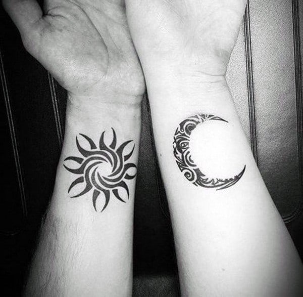 Matching wrist tattoos of a tribal sun and moon, symbolizing balance, duality, and the powerful connection between opposites in love.