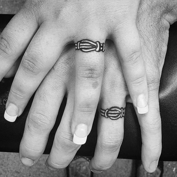 Matching tattooed wedding bands on ring fingers, featuring a symbolic design that represents eternal love and unbreakable commitment.