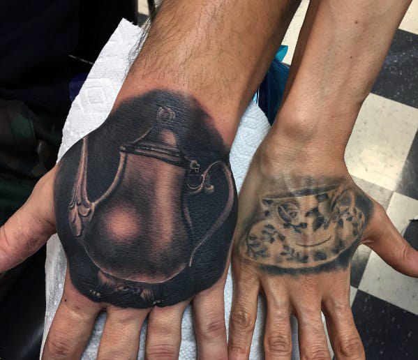 Matching hand tattoos of a teapot and teacup, symbolizing a perfect pairing and shared moments of warmth and comfort.