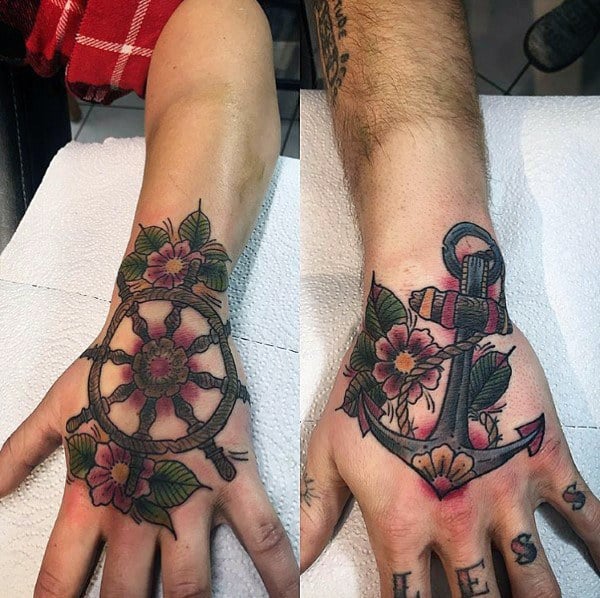 Matching hand tattoos of a ship wheel and anchor adorned with flowers, symbolizing guidance, stability, and a love that keeps each other grounded.