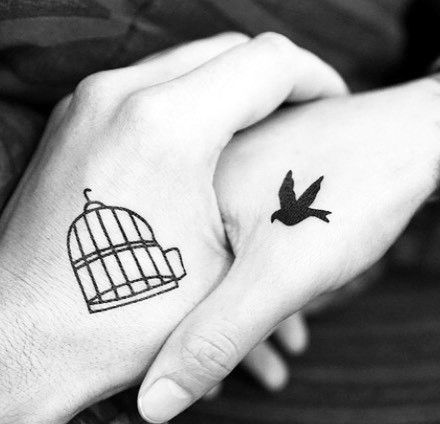 Matching hand tattoos of a birdcage and a flying bird, symbolizing freedom, trust, and love without constraints.