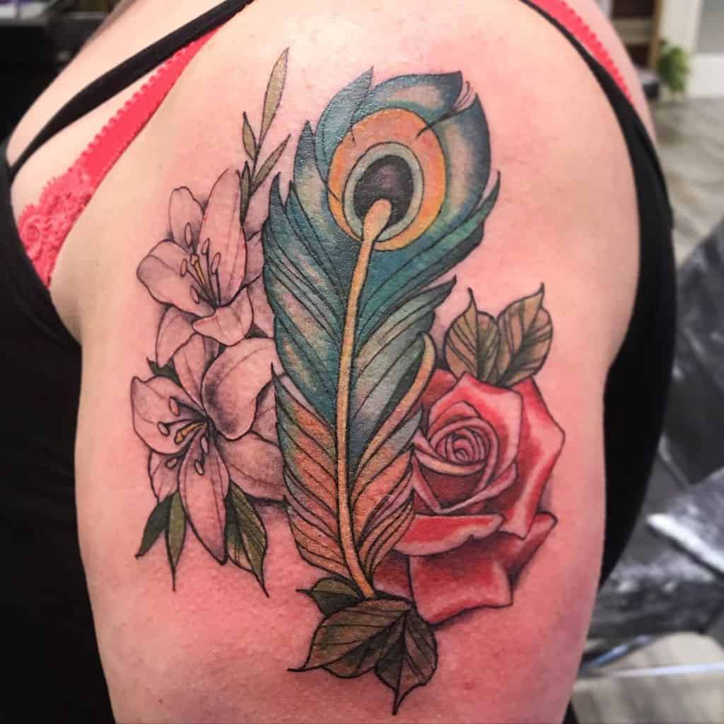 Colorful upper arm tattoo featuring a vibrant peacock feather, a red rose, and black-and-grey lilies with intricate shading and fine details.