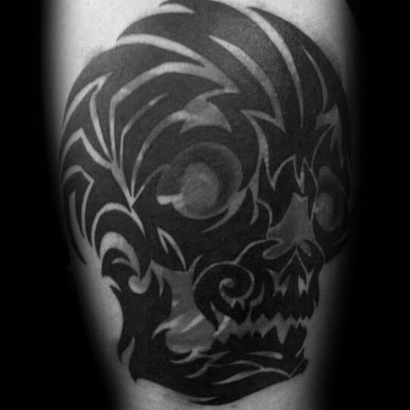 Tribal skull tattoo in solid black ink with sharp, abstract patterns forming a fierce and stylized skull design on the upper arm.