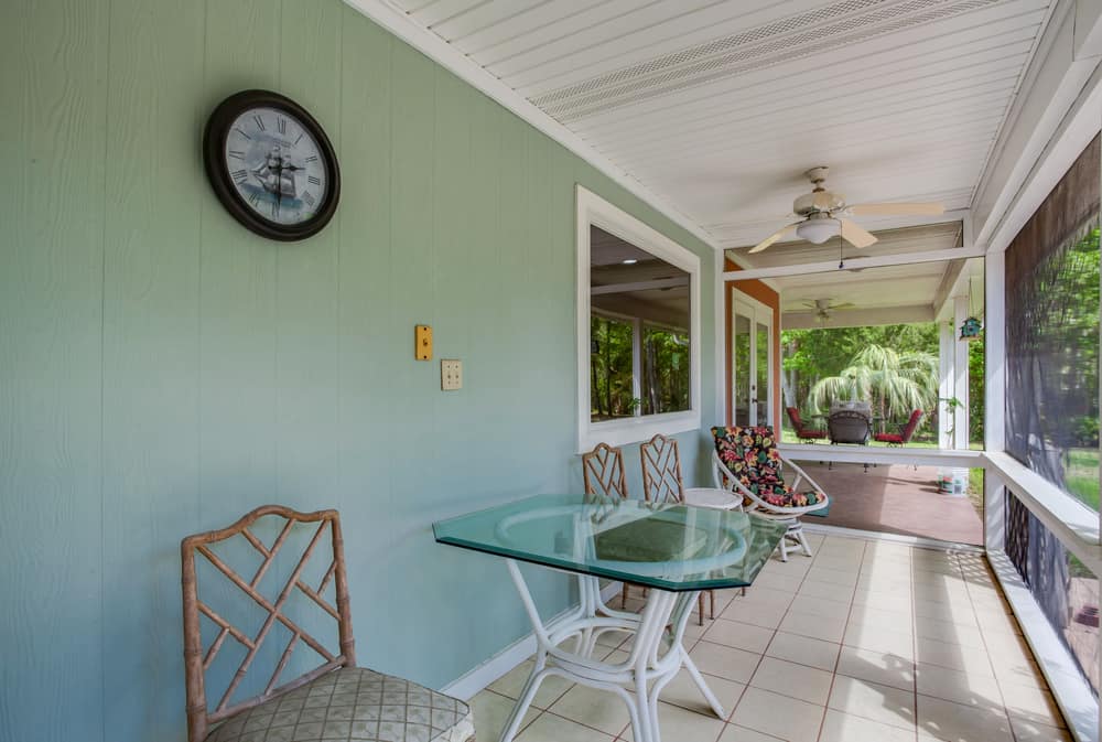 green accent wall covered enclosed patio ceiling fan glass tabletop chairs wall clock