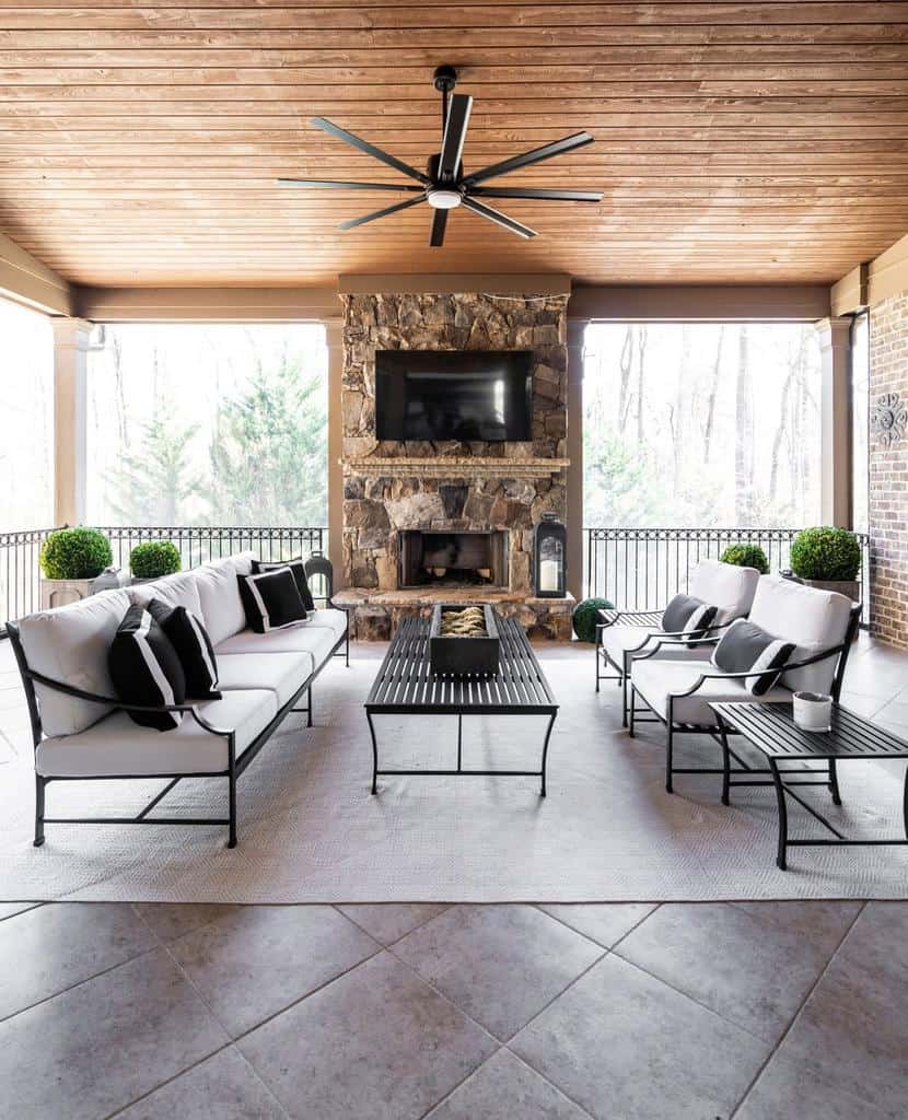 large covered patio wood ceiling stone fireplace black metal outdoor furniture ceiling fan and light
