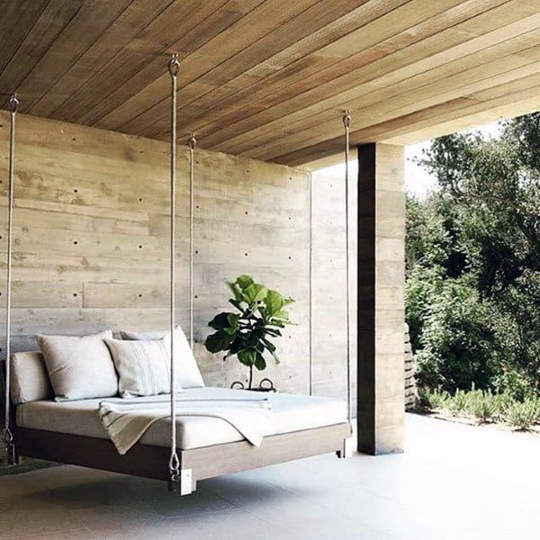 Minimalist hanging bed with white cushions, sleek rope supports, and a wooden patio ceiling.