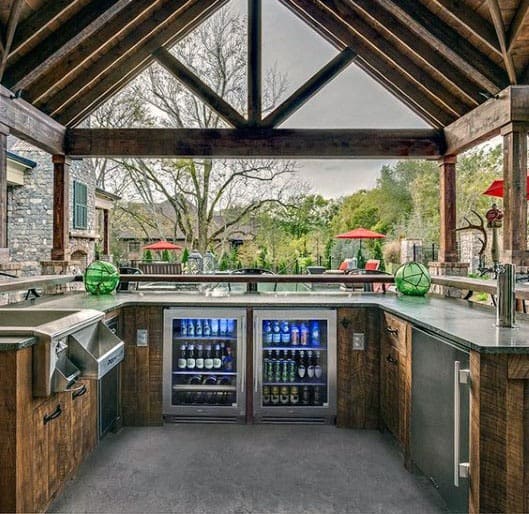 Rustic outdoor pavilion bar with modern kitchen appliances, beverage coolers, and a scenic view.