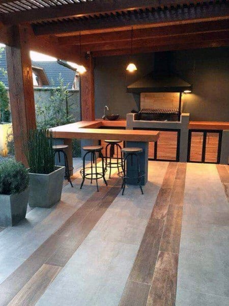 Sleek outdoor BBQ bar featuring wooden countertops, steel stools, and a shaded seating space.