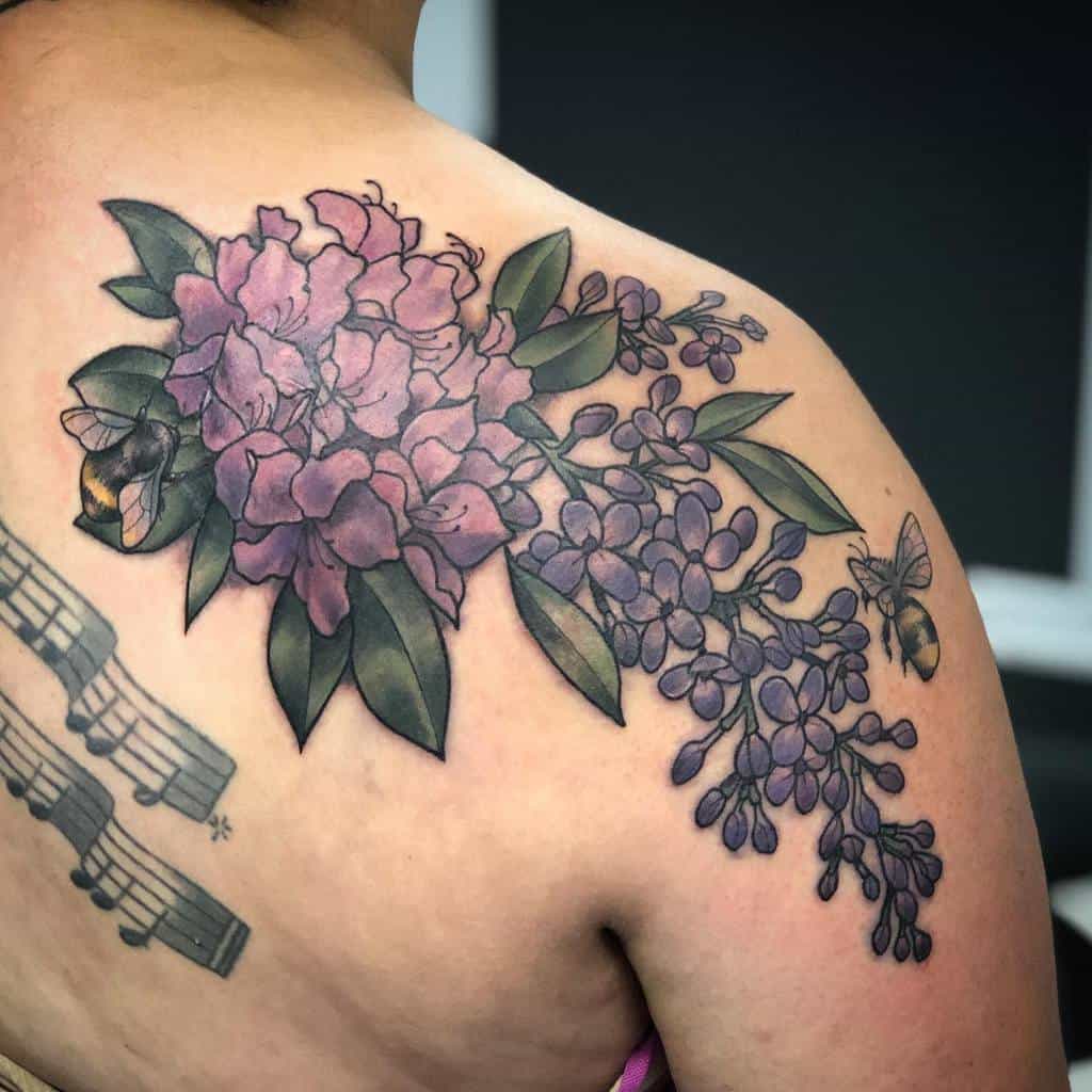 Large floral shoulder tattoo featuring lilac and peonies with deep purple hues, lush green leaves, and bees hovering nearby.