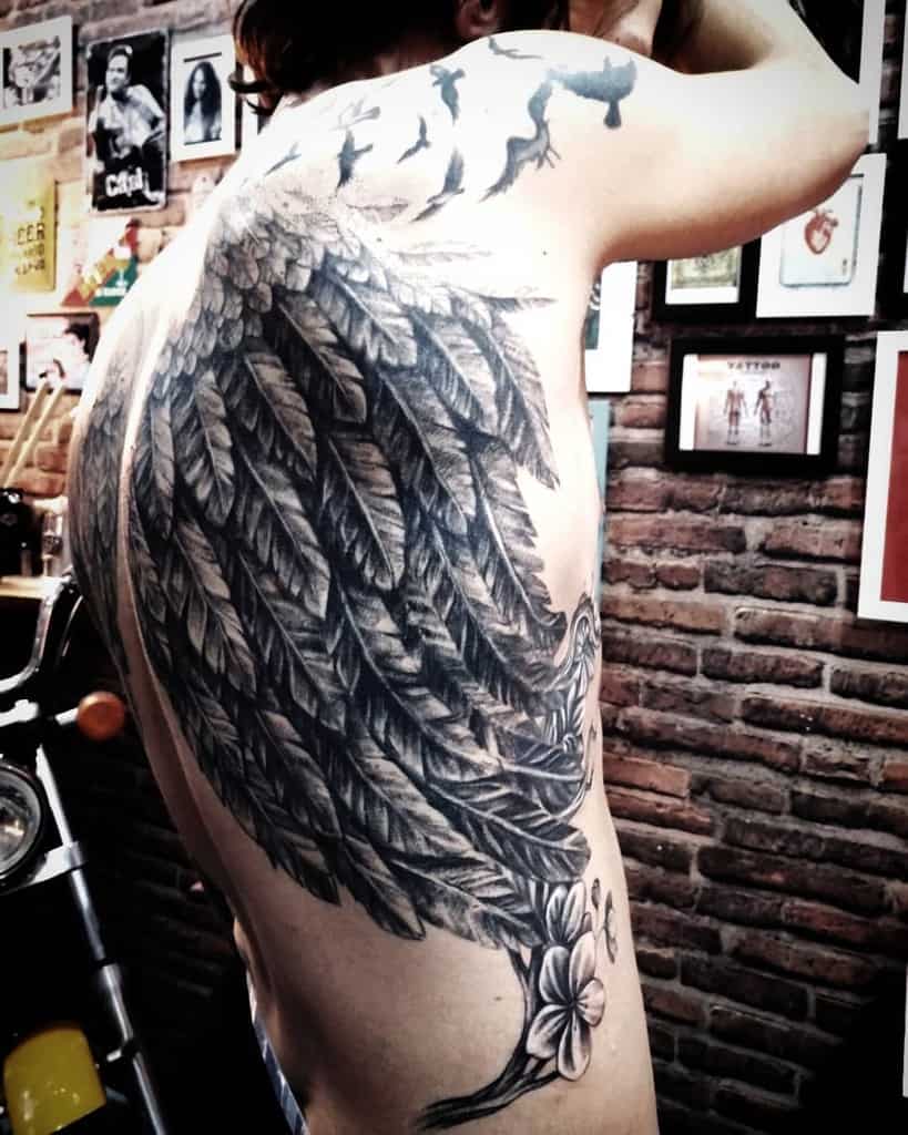 A large angel wing tattoo with birds above and flowers below