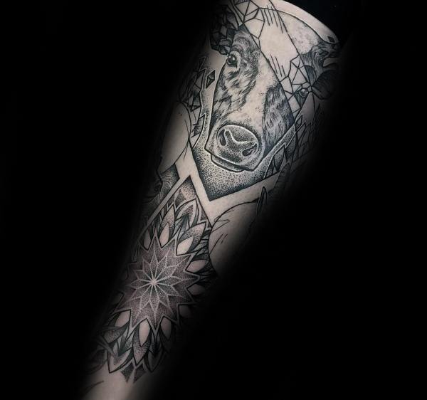 Geometric black and grey cow tattoo with fine linework, abstract shapes, and a detailed mandala on the forearm.
