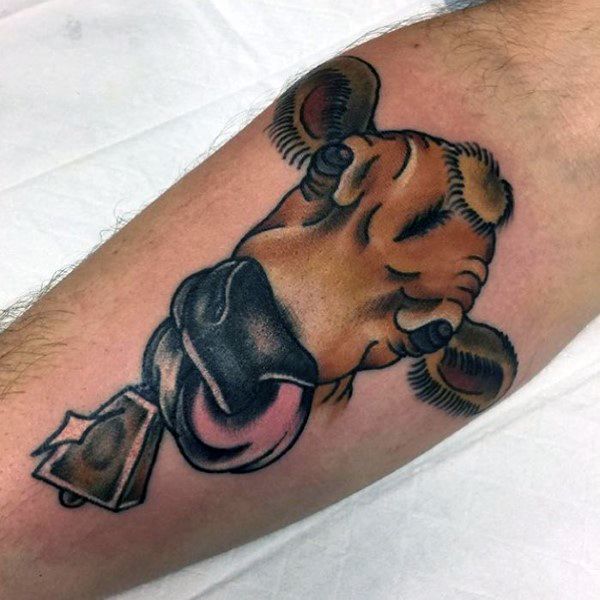 Playful cow tattoo with cartoon-style shading, tongue sticking out, and a bell under the chin on the forearm.