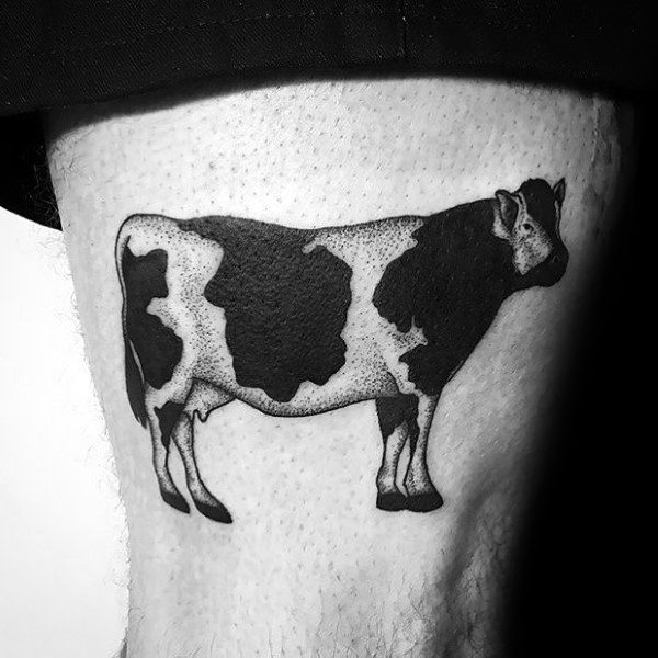 Minimalist black and grey tattoo of a standing cow with bold spots, placed on the upper thigh.