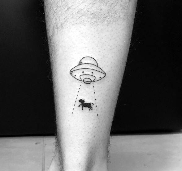 Minimal UFO and cow abduction tattoo on calf, featuring dotted beam lines and a small silhouette of a cow being lifted.
