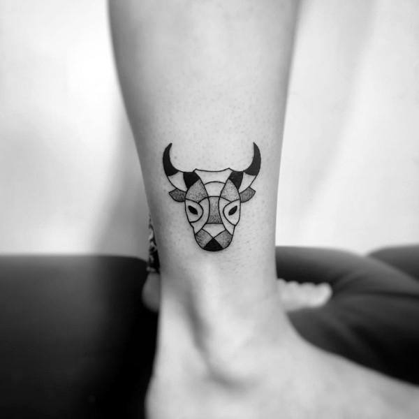 Small geometric cow head tattoo on the lower leg, featuring bold black shapes and symmetrical modern design.