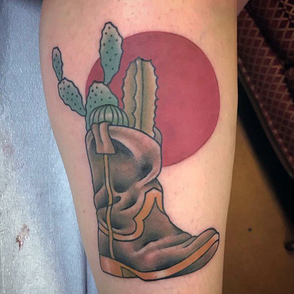 Tattoo of a cowboy boot with cacti growing from it, set against a red sun, symbolizing resilience, Western heritage, and desert life.
