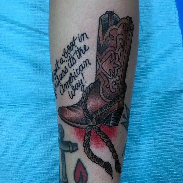 Tattoo of a detailed cowboy boot with a rope and bold lettering stating "Put a boot in that ass, it's the American way!"