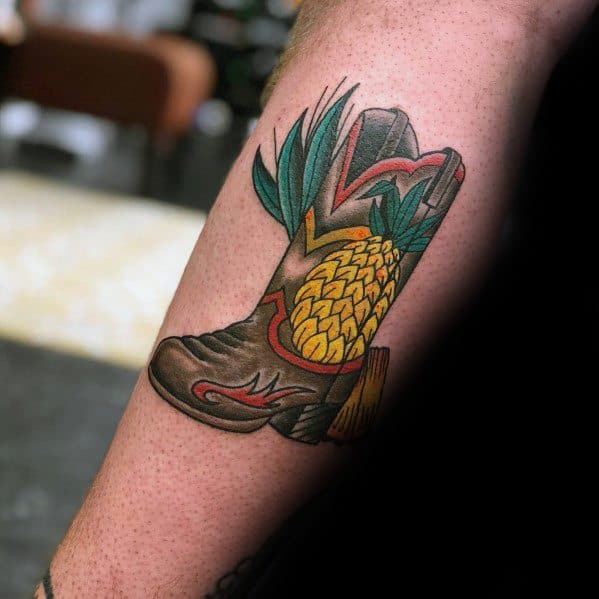 Tattoo of a cowboy boot with a pineapple and green leaves, combining Western style with a tropical twist for a bold and unique design.