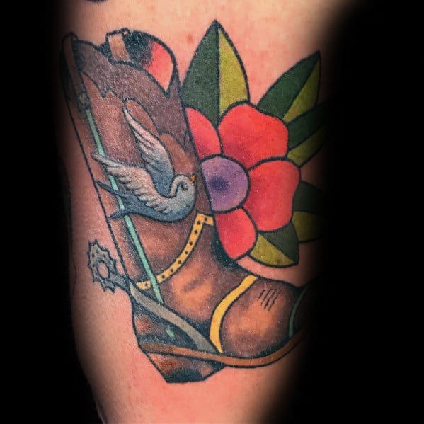 Tattoo of a cowboy boot with a swallow, spur, and vibrant flower, blending Western tradition with classic Americana tattoo style.