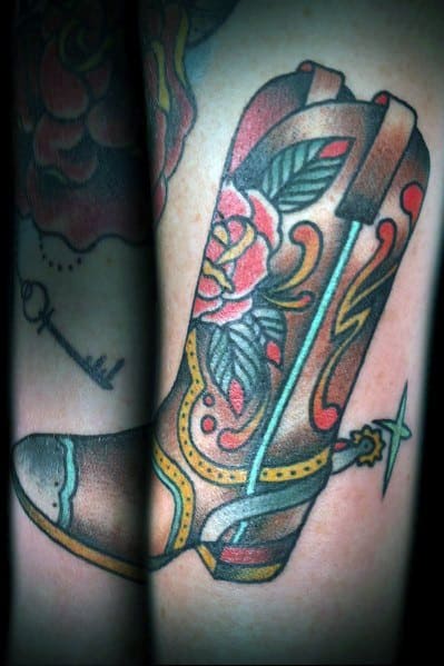 Tattoo of a detailed cowboy boot with floral patterns and a spur, blending Western heritage with bold, colorful traditional tattoo style.