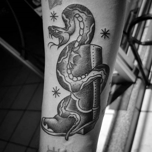 Tattoo of a cowboy boot with a coiled snake wrapped around it, symbolizing danger, resilience, and the untamed spirit of the Wild West.