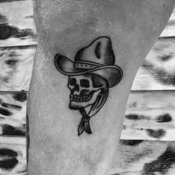 Tattoo of a small cowboy skull wearing a hat and a bandana, done in black and gray shading for a classic Western-style look.