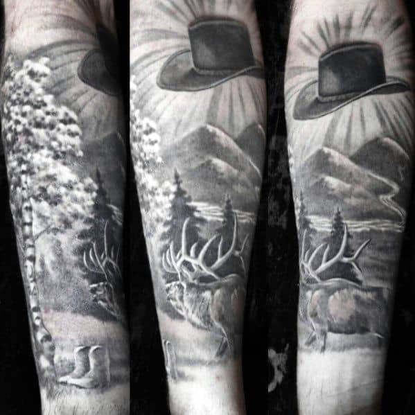 Black and gray tattoo of a scenic wilderness featuring mountains, trees, an elk, and a cowboy hat in the sky with rays of light.