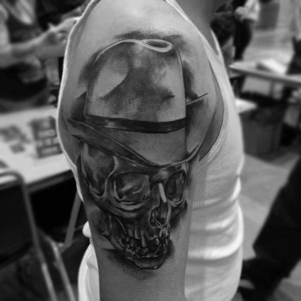 Realistic black and gray tattoo of a skull wearing a fedora, with detailed shading and depth, creating a dark and mysterious look.
